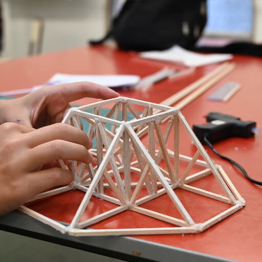 Unas manos ensamblando una estructura en varillas de madera balsa