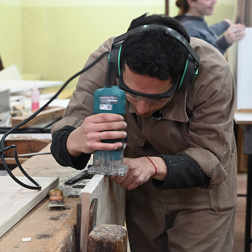 Estudiante trabajando con una lijadora sobre el canto de una pieza de madera